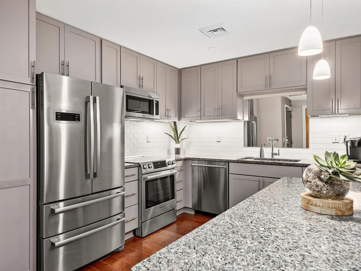 A contemporary kitchen scene with stainless steel appliances, a generous granite countertop, a chic subway tile backsplash, and a touch of greenery from a potted plant. The space is designed for cooking, entertaining guests, and hosting family gatherings, emphasizing both practicality and style.