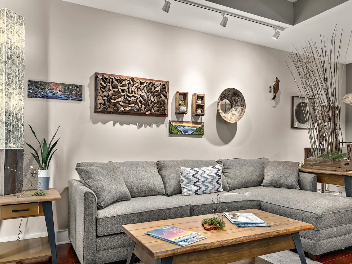 A modern living area with a sectional sofa, wall art, a coffee table topped with magazines, and decorative branches. The ambiance is calm and inviting, ideal for relaxing after arrival and evoking the comforts of a private residence.