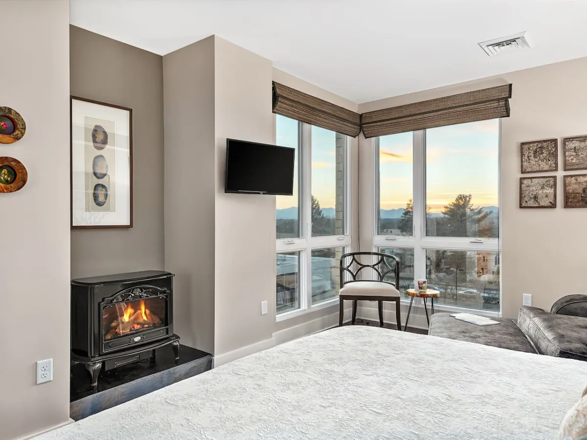 A warm, inviting living space featuring a comfortable chair beside a fireplace, large windows that frame city or mountain views, and tasteful artwork on the wall. The arrangement encourages casual conversation, relaxation, and enjoying sunsets from the comfort of the living room, reinforcing an elevated downtown lifestyle.